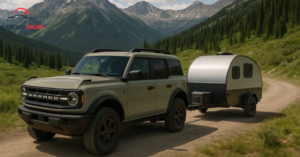 A Ford Bronco towing a small off-road camper on a dirt road through the mountains.